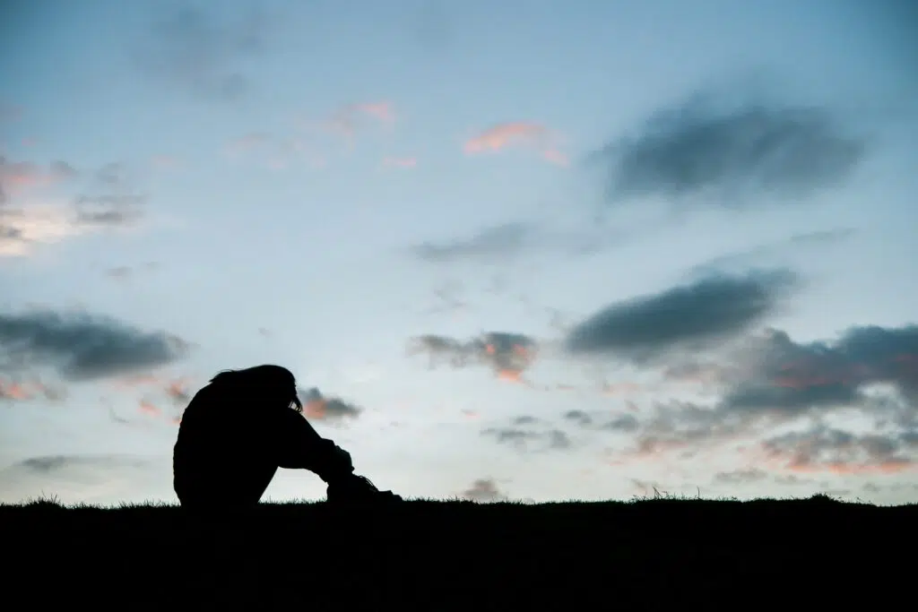 Silhouette of sad woman head on knees at sunset.