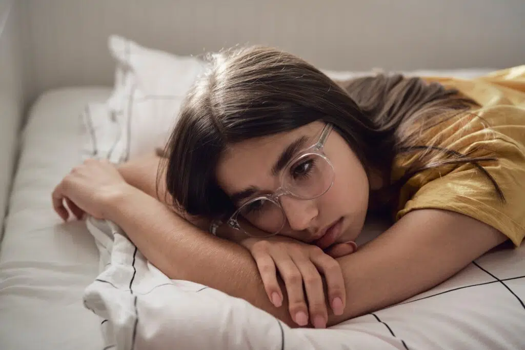 Sad caucasian teenage girl lying on bed and looking away with anxiety