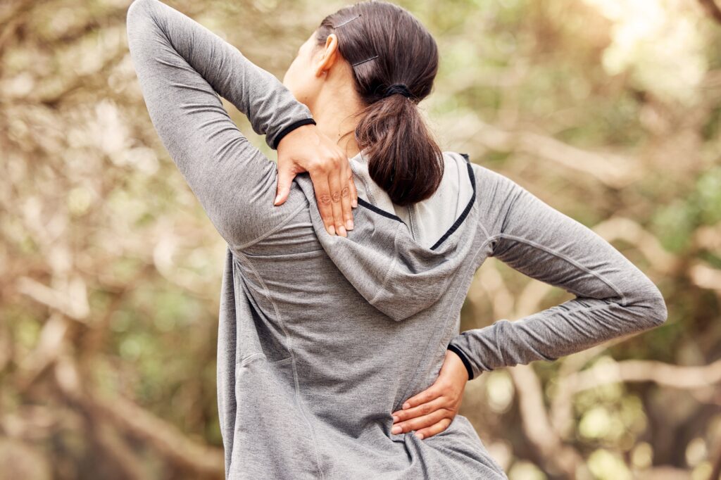 Rearview shot of a woman experiencing back pain while working out in nature