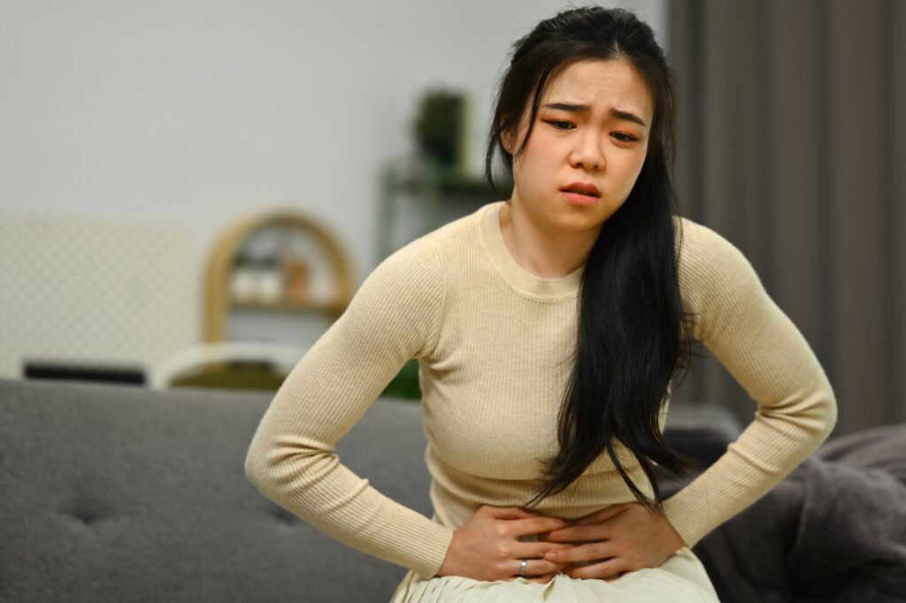 Young woman sitting on sofa at home suffering from stomachache, diarrhea or indigestive problem.