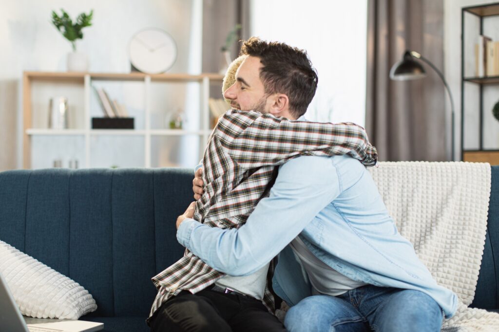 Same sex couple sitting on couch in strong hugs